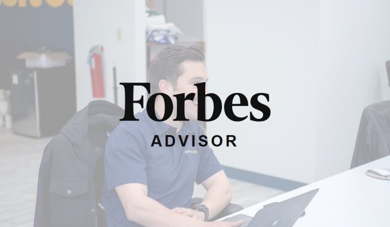 Forbes Advisor logo over a SmartSites SEO strategist at his desk